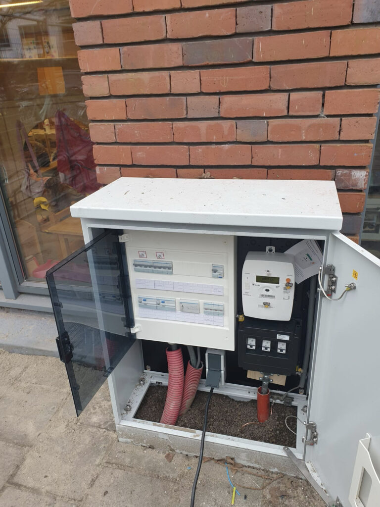 13 De straatkast met de twee geribbelde buizen met stroom van het dak, en de rode buis met onze zonnestroom naar het elektriciteitsnet